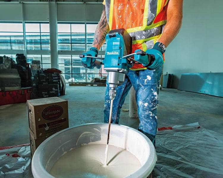 Construction worker operating a large Makita Mixer to mix concrete on the jobsite, showcasing the tool's strength and versatility