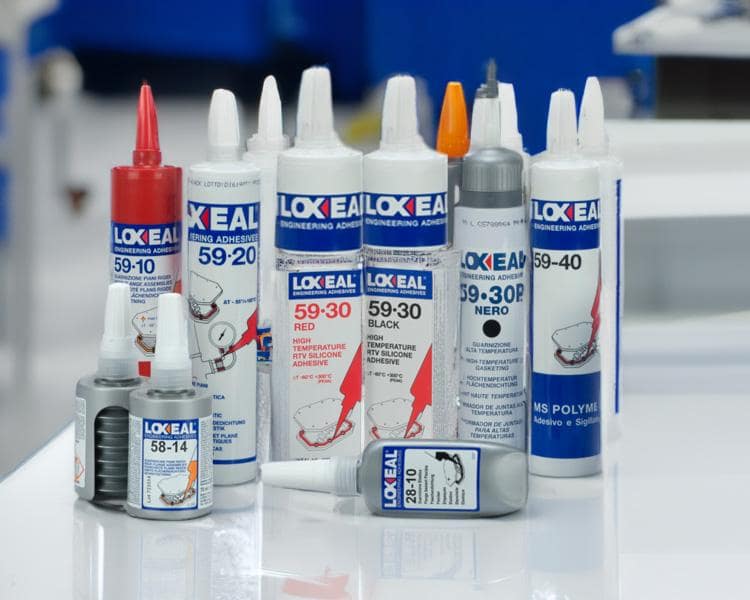 Tubes and bottles of Loxeal adhesive products arranged on a table, with focus on items in the foreground against a blurred blue background, highlighting product quality