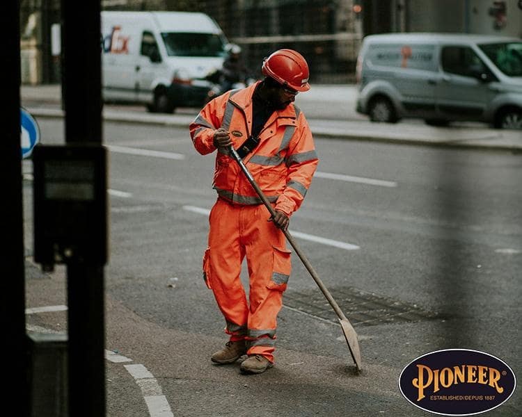 Construction worker in Pioneer orange reflective gear using a hoe on a city street, showcasing safety gear and work in progress with Pioneer logo