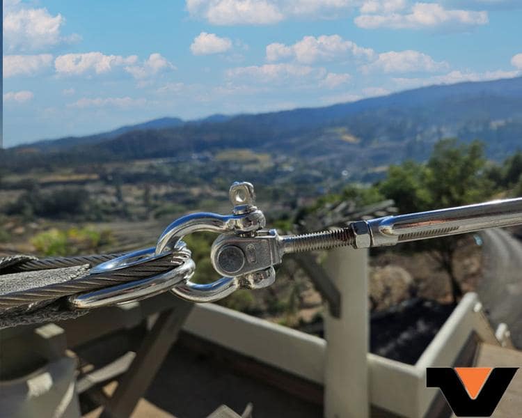 Clasp turnbuckle holding a wire and steel cables made by Vanguard Steel, adjustable and positioned in a scenic outdoor vista for industrial use.